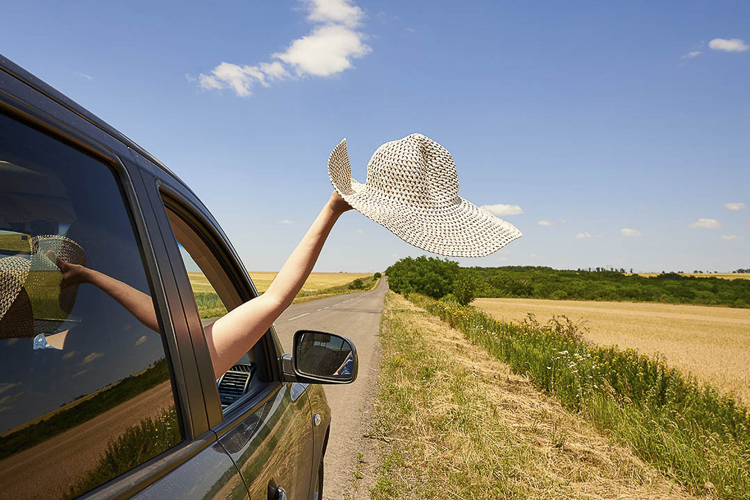 a women's arm hanging out of a car window with a hat in her hand