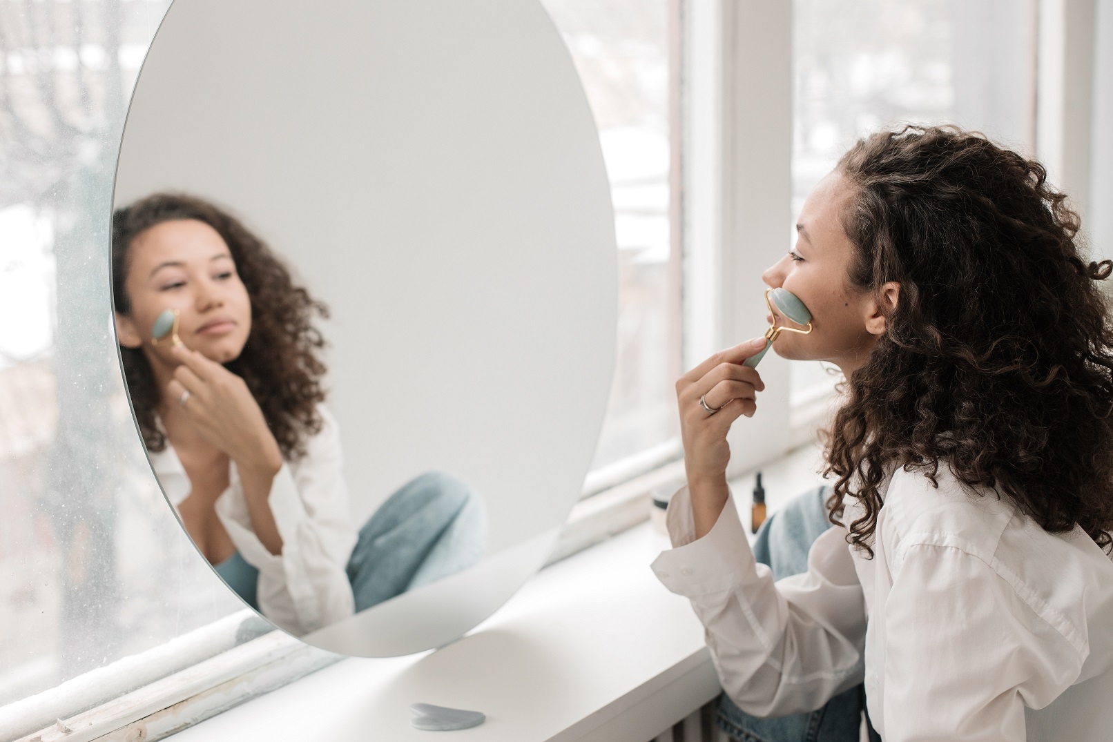 a women using a jade roller in front of a mirror